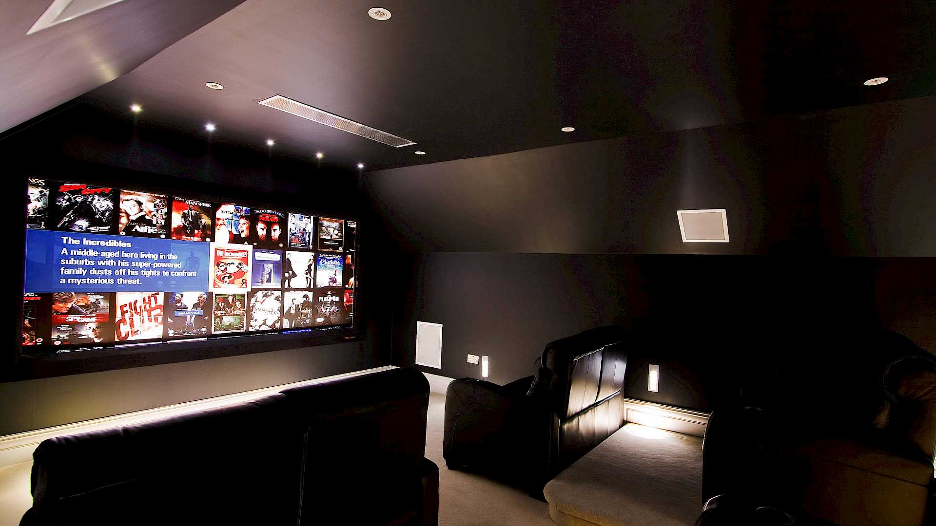 Shows home cinema from side left, with comfortable cinema seating and large acoustically transparent movie screen.