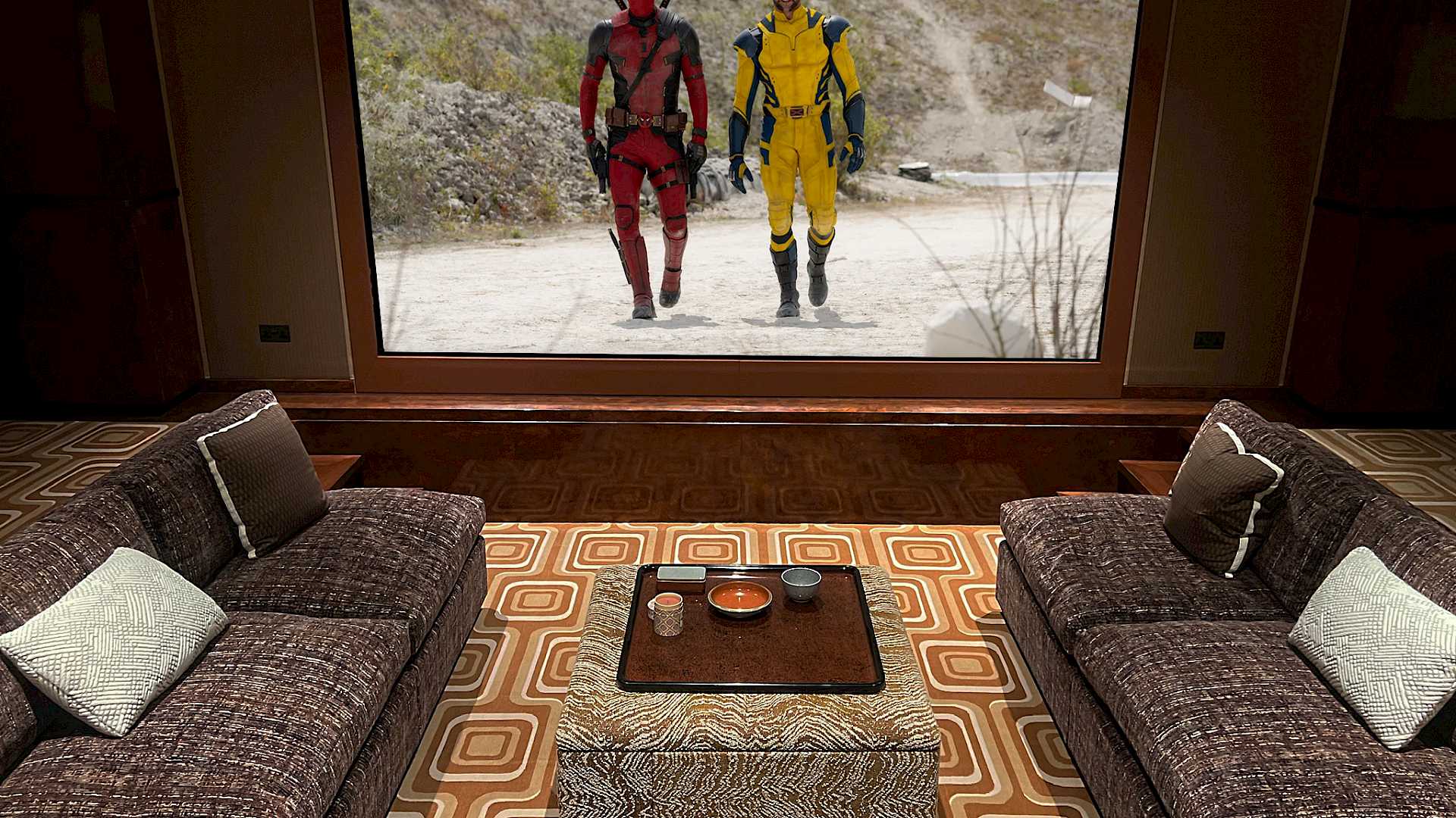 Shows home cinema screen from seating position, with coffee table and Marvel film on screen.