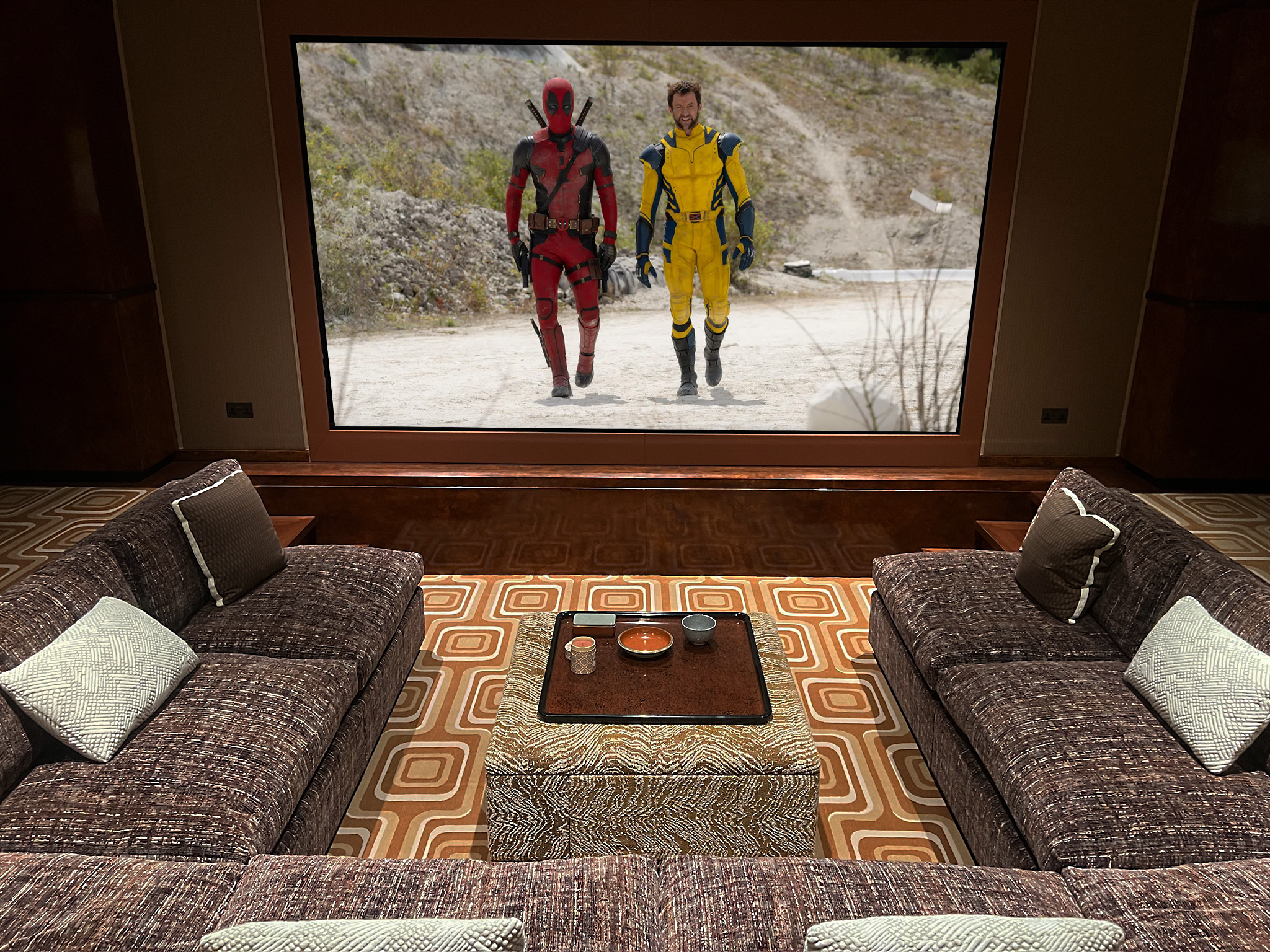 Shows home cinema screen from seating position, with coffee table and Marvel film on screen.